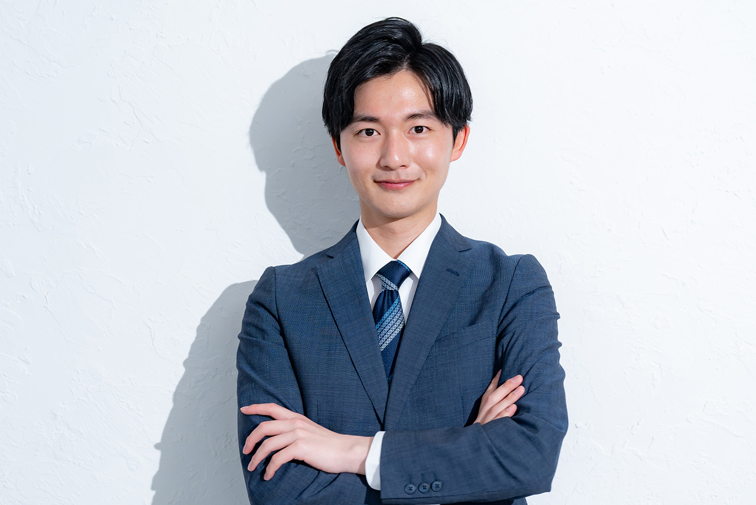 腕を組んで微笑むスーツ姿の男性